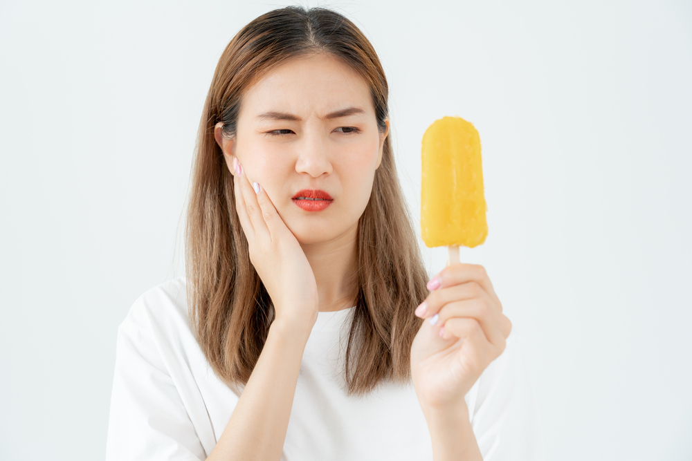 woman wincing and touching side of her face while looking at orange Popsicle